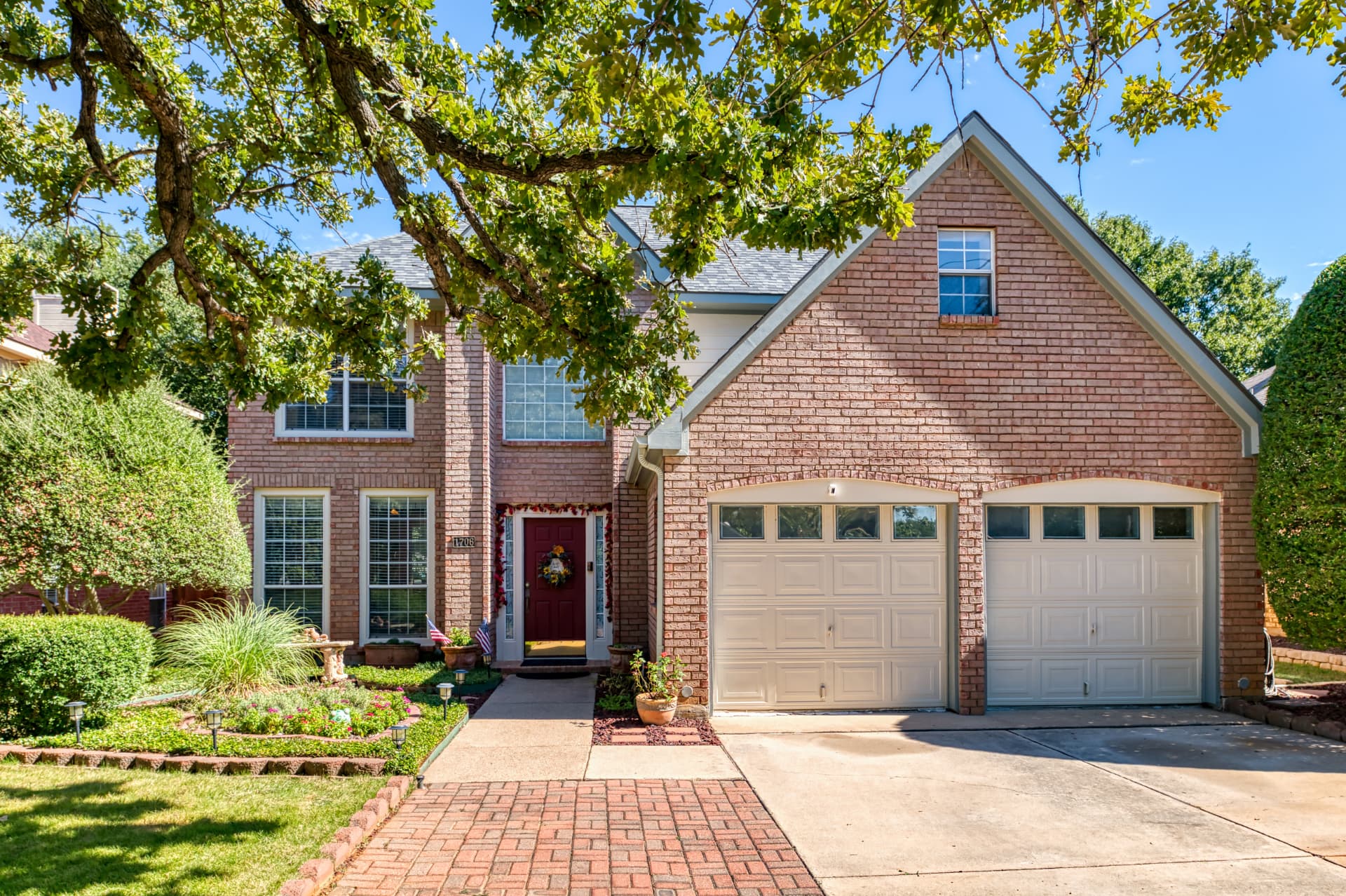 Front exterior of the two-story brick home at 1706 Hood Lane with a two-car garage, brick paver walkway and mature landscaping