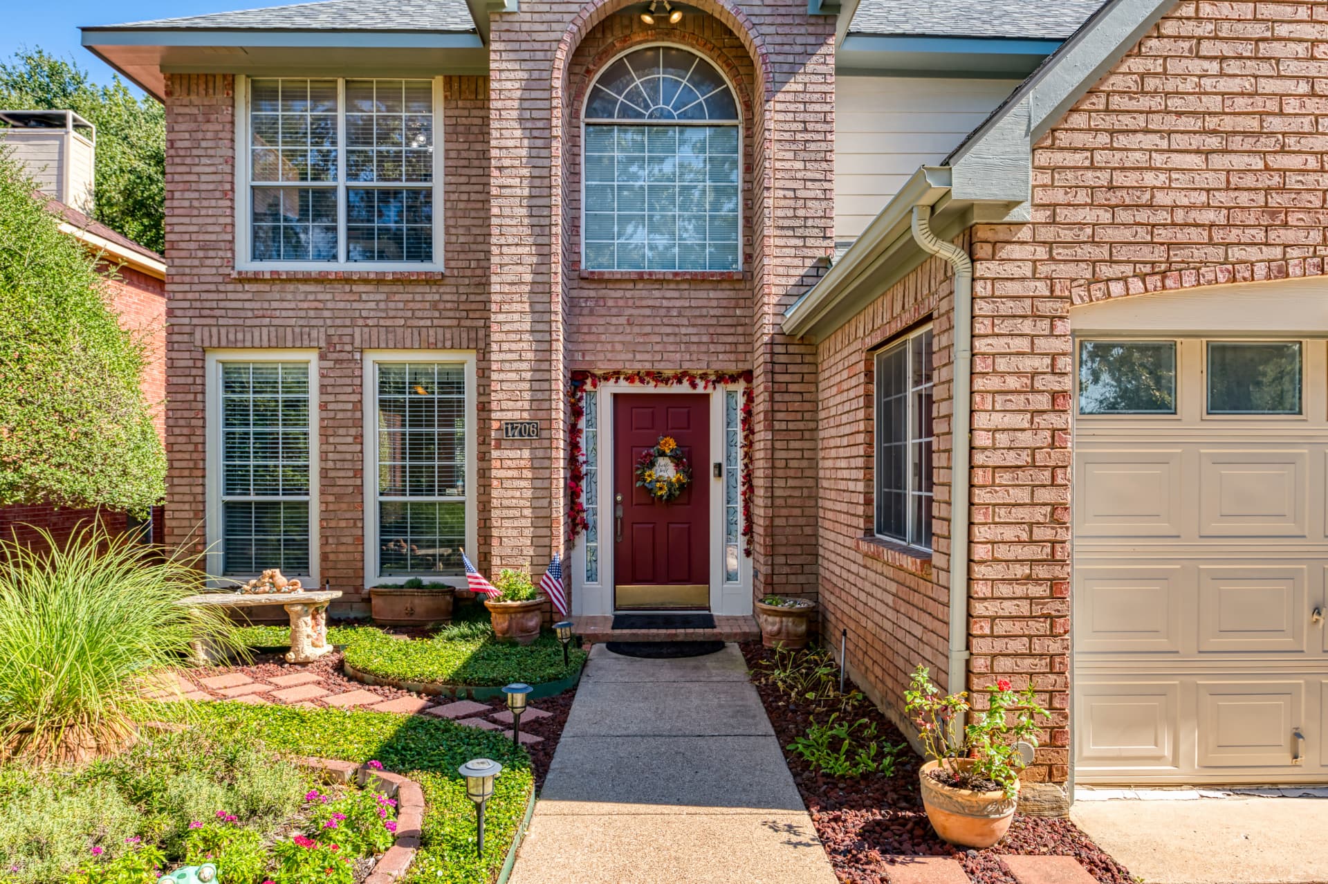 Arched brick front entryway with a burgundy door, seasonal wreath and concrete walkway